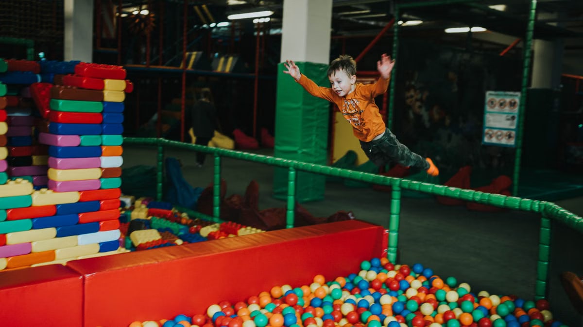 A joyful child jumps into a colorful ball pit at an indoor playground, capturing fun and excitement.